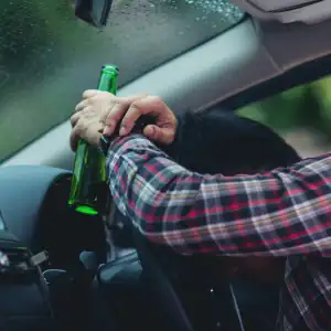 Drunk driver holding a beer bottle behind the wheel, risking a serious accident